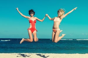 women in bikinis jumping on the beach