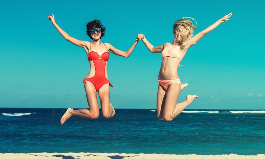 women in bikinis jumping on the beach